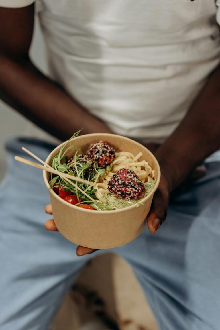 A close-up of a healthy vegan meal featuring noodles and sesame balls in a biodegradable bowl.