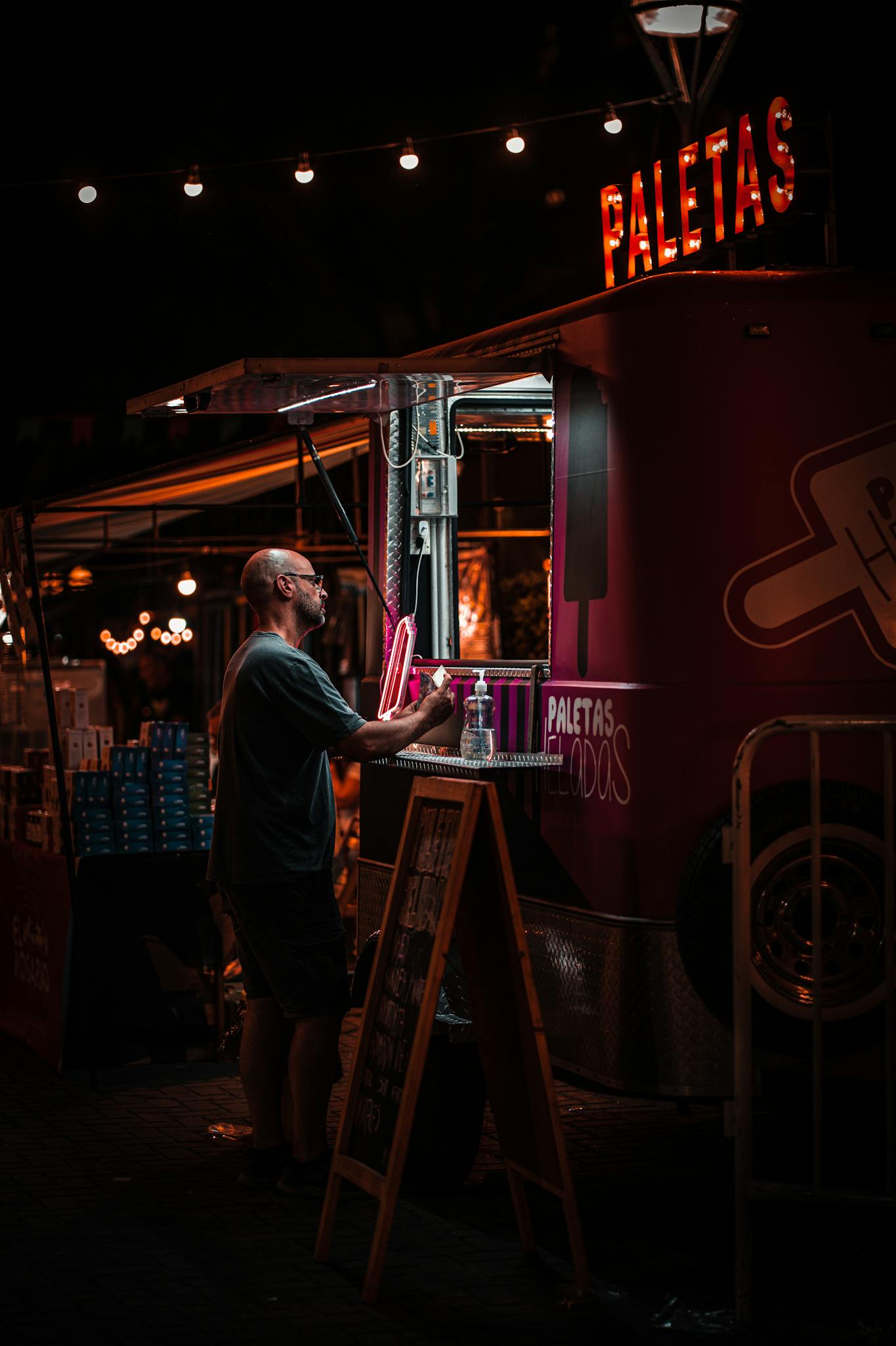 Nighttime view of a food truck selling paletas with a customer ordering under ambient lighting.